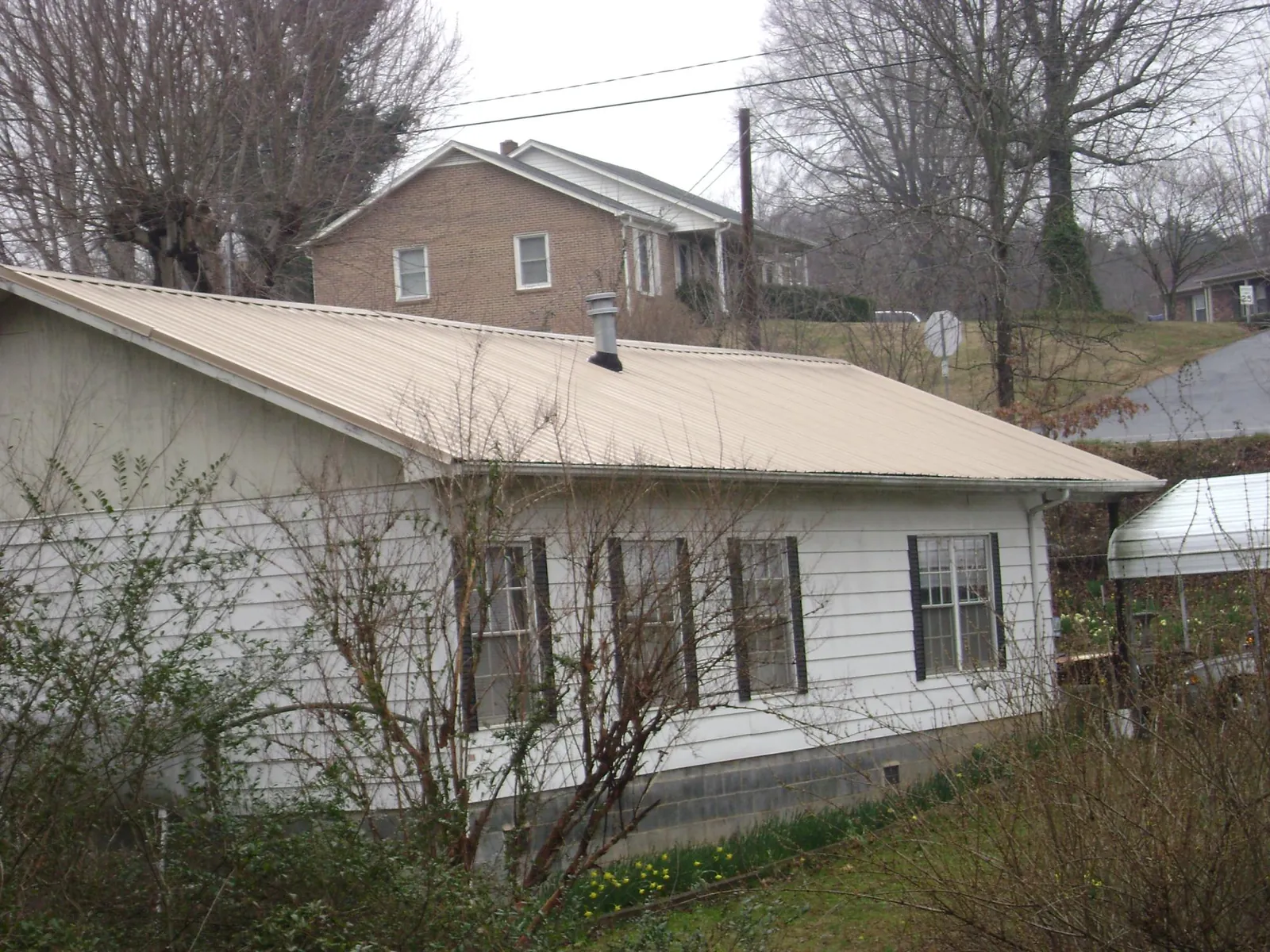 Tan metal roof on a white sided house set into a hillside — Commercial Roofing by Roofing Brothers in Mcminnville
